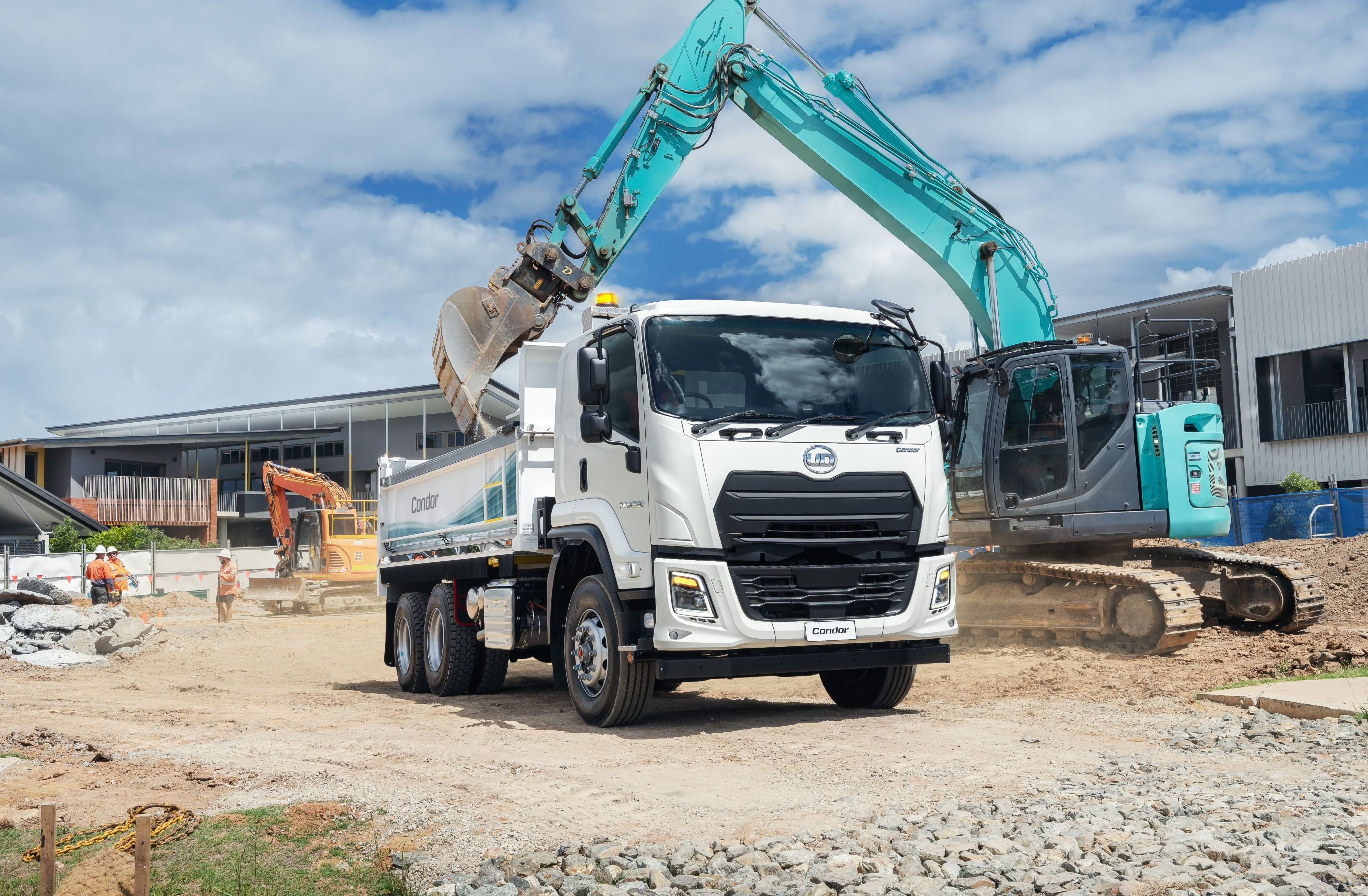 Dump truck being loaded with dirt by a teal excavator at a construction site.
