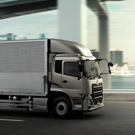 Silver delivery truck driving on city highway under bridge.