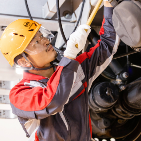 Technician in helmet and gloves inspecting machinery under bright lights.