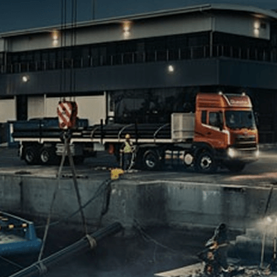 Vragmotor met rooi kajuit by industriële perseel in die aand.