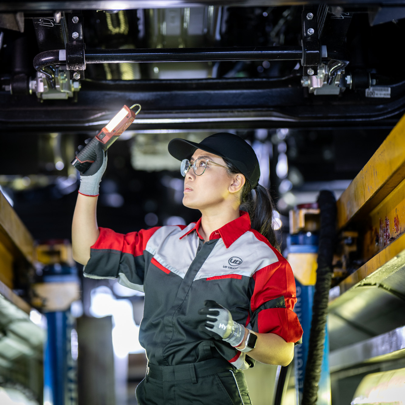 Mechanic in uniform inspecting vehicle underside with a flashlight.