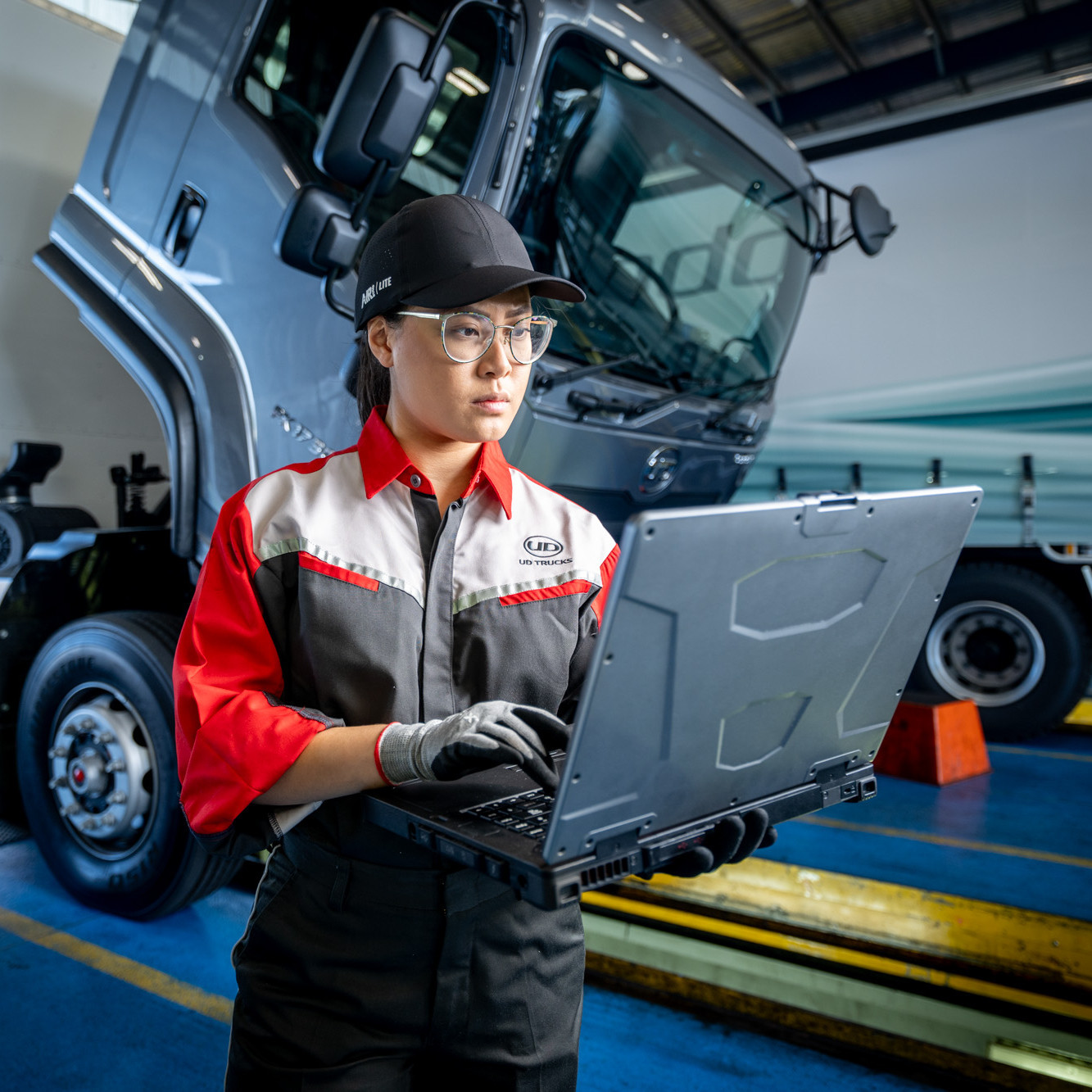 Mechanic in uniform using a laptop beside a large truck in a workshop.
