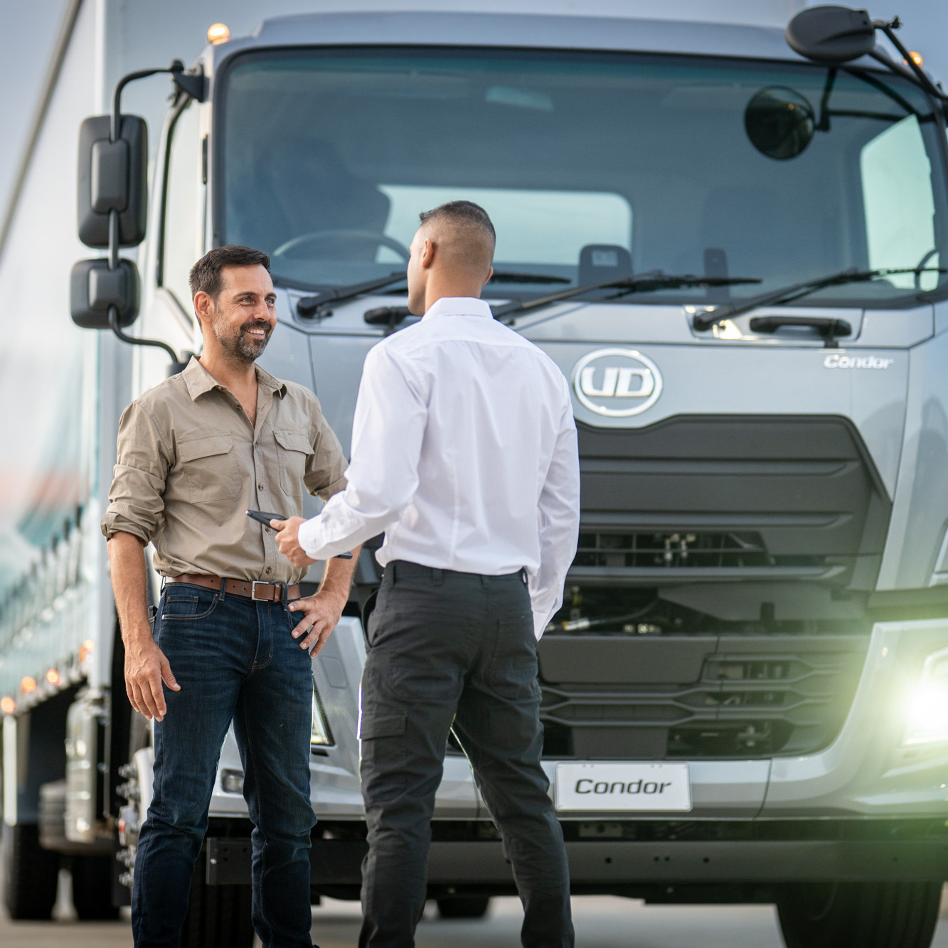 Two men talking in front of a large silver truck.