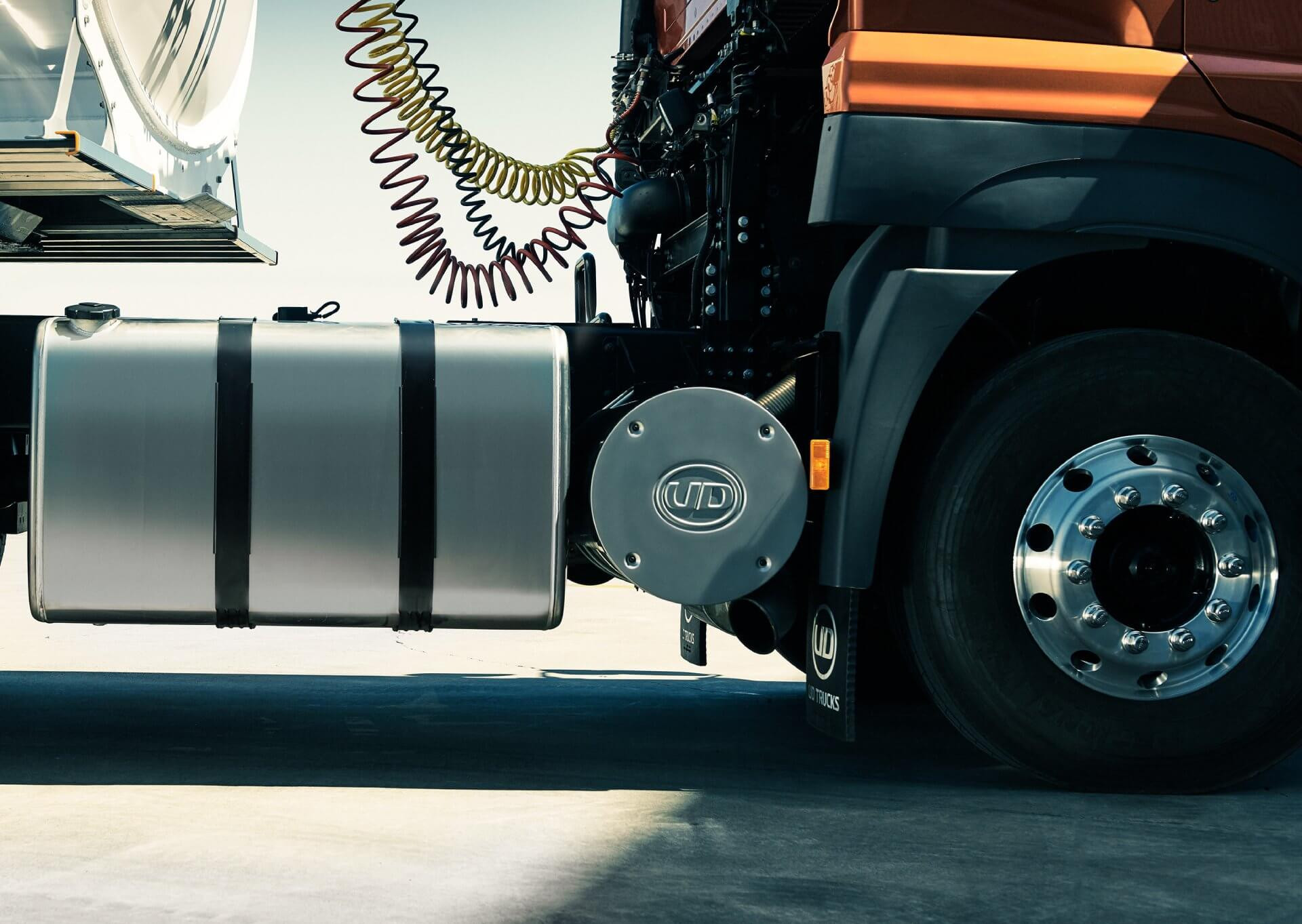 Bagian samping depan truk dengan ban besar dan tangki bahan bakar logam.