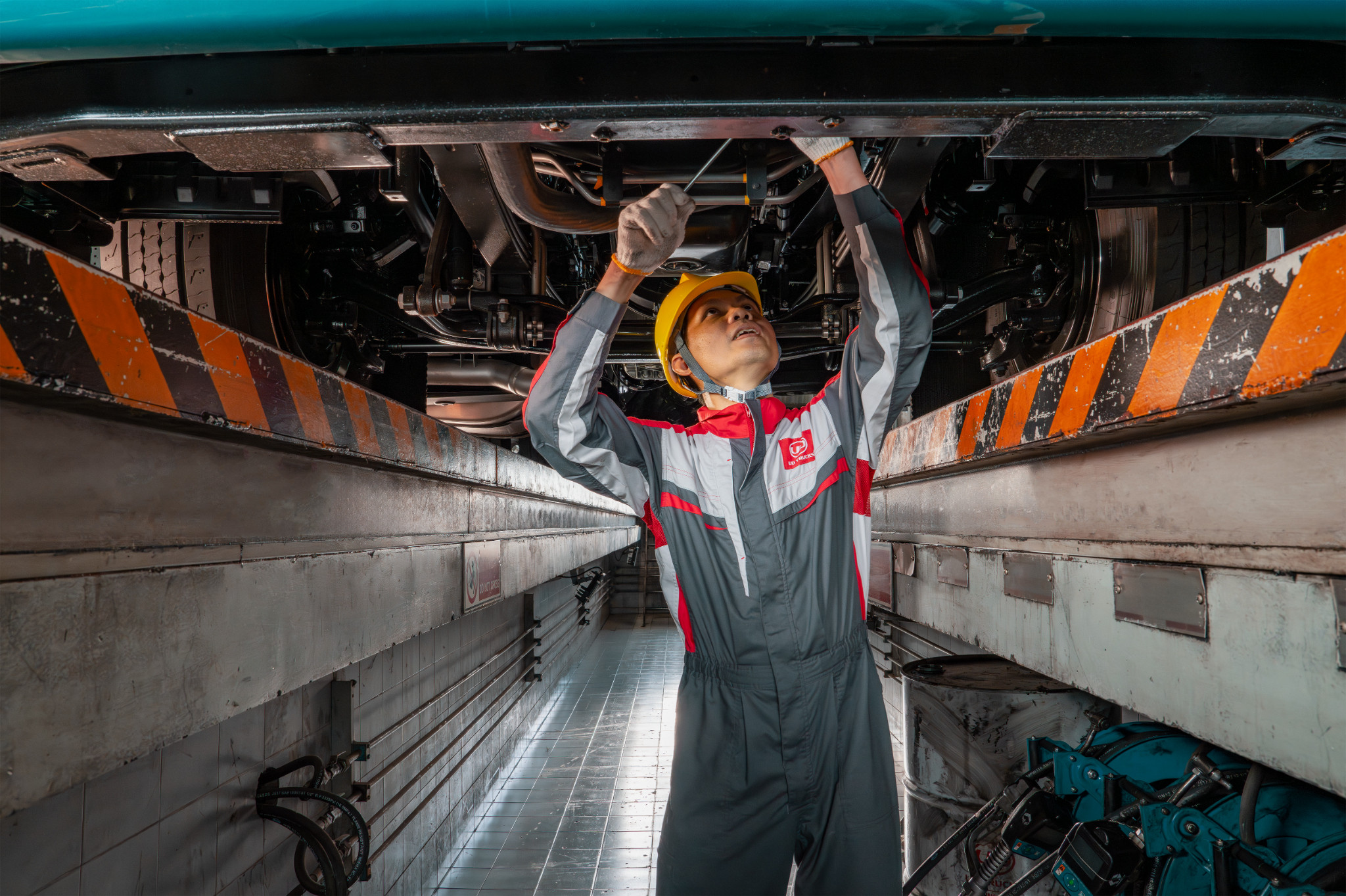 Mechanic in a jumpsuit and helmet repairing machinery under a large vehicle.