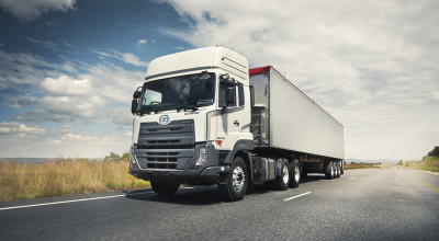 White semi-truck driving on a highway under a partly cloudy sky.
