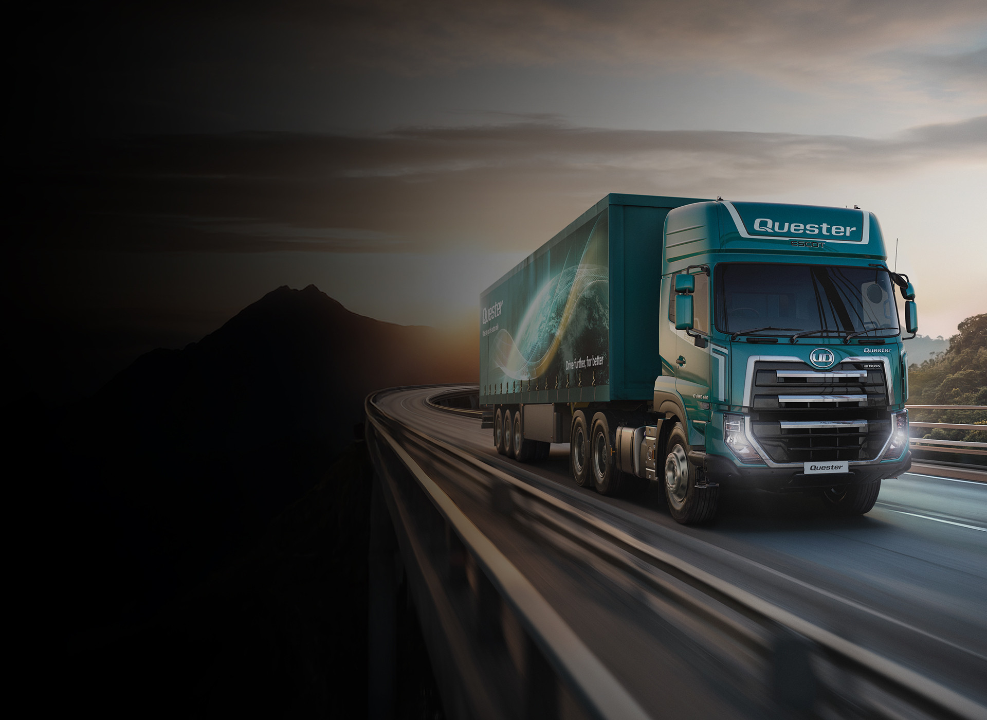 Vragmotor ry op snelweg by sonsondergang, berge in die agtergrond.