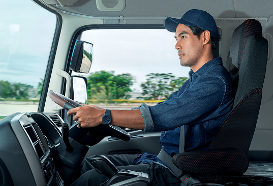 Man in a blue cap driving a truck on a sunny day.